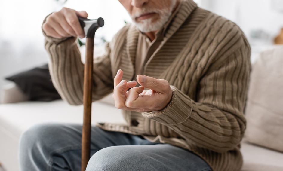 senior man with parkinson disease holding walking cane while sitting on couch