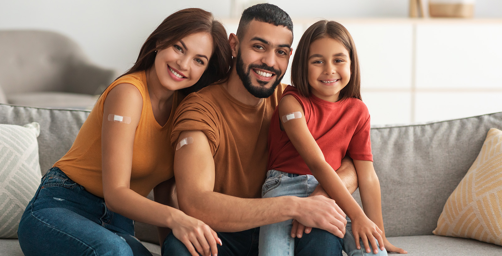 Mom, dad, and child sit on a sofa and show off their flu shot band aids