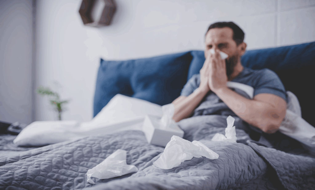 Man in bed with fly surrounded by tissues and blowing his nose.