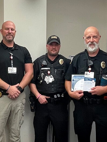Three security guards stand next to each other and one holds the employee of the month certificate