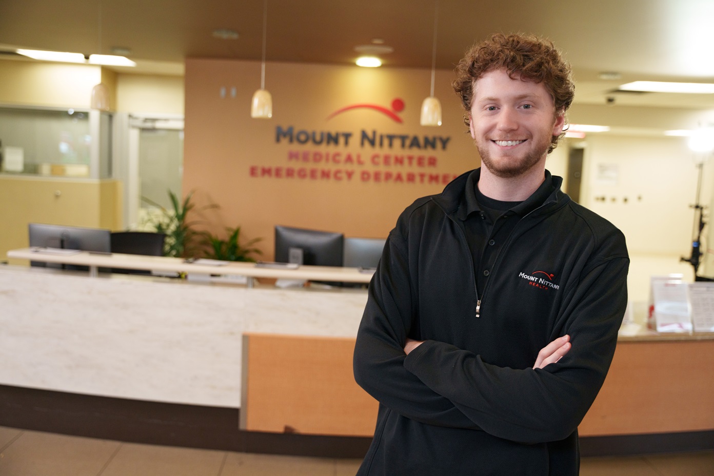Smiling Mount Nittany Health Employee stands in front of reception desk.
