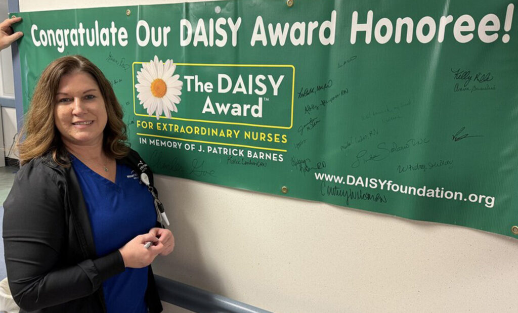 Kate Lenhart poses with the DAISY Award green banner sign