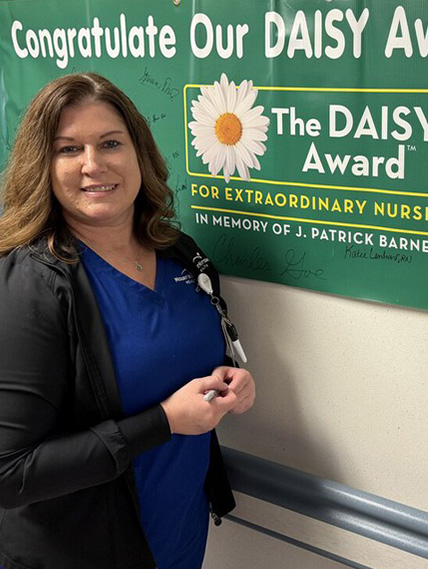 Kate Lenhart poses with the DAISY Award green banner sign