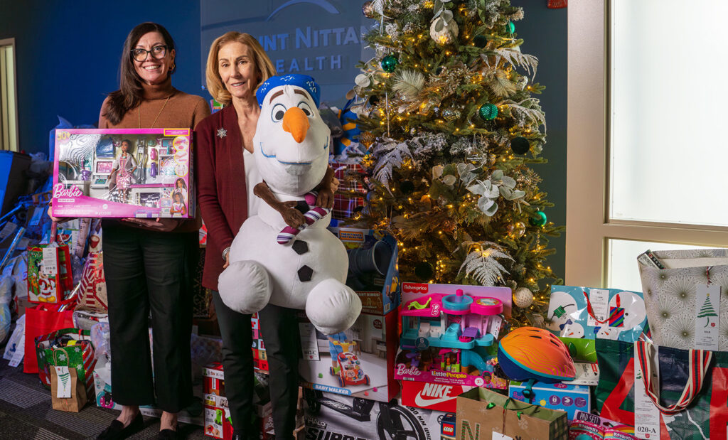 Two women hold toys in front of a Christmas tree