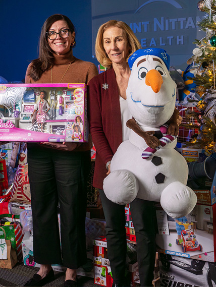 Two women hold toys in front of a Christmas tree