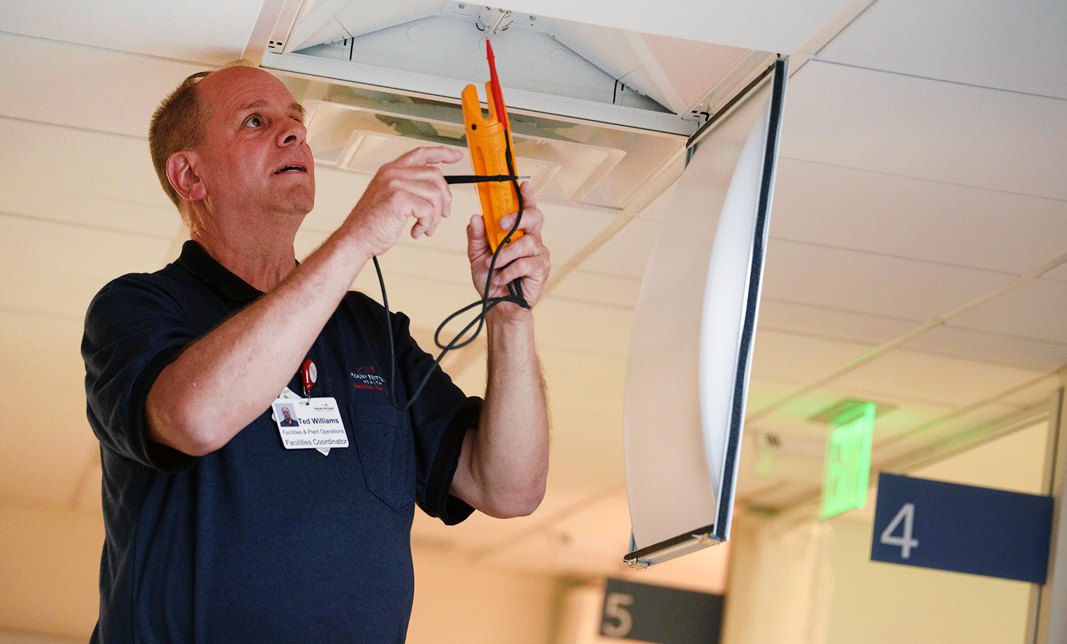 Ted from Facilities stands on a ladder and changes a lightbulb