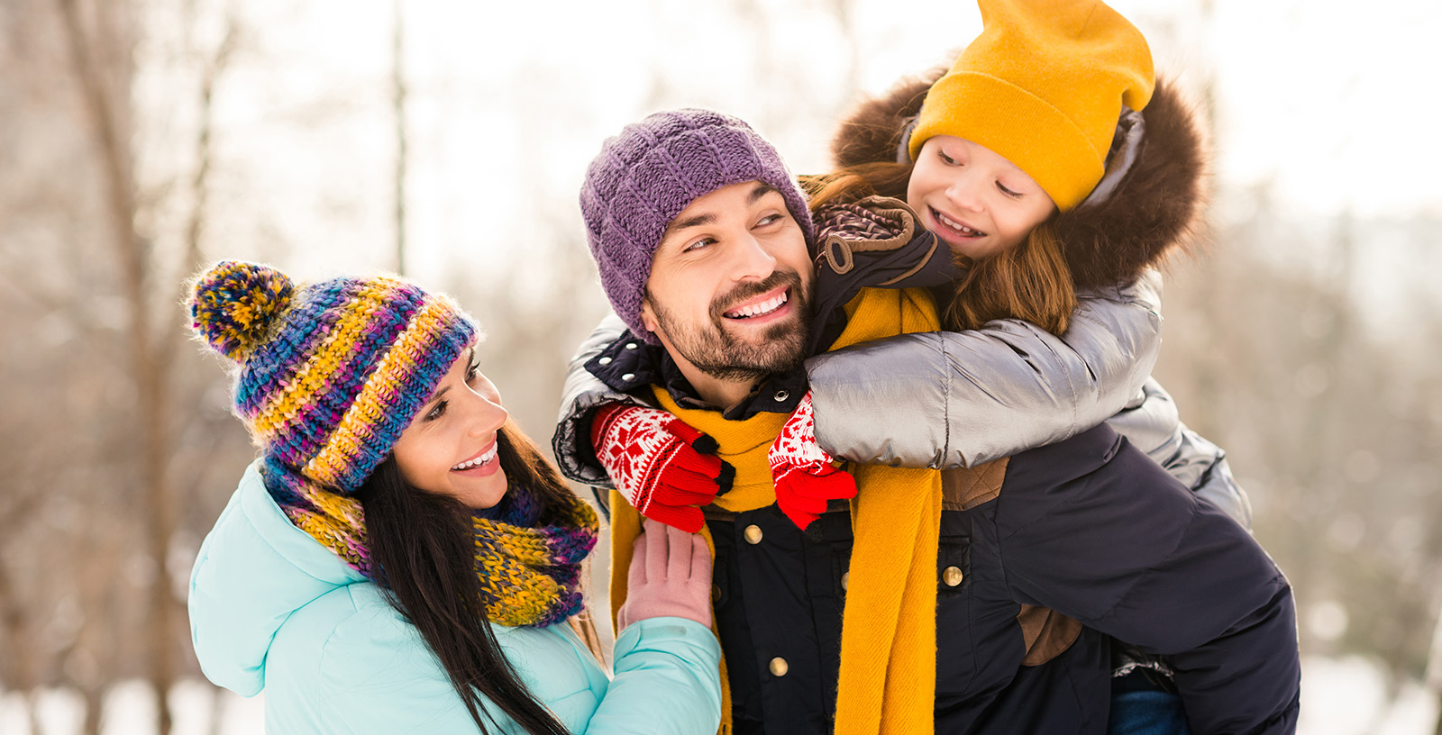 Kid is playing with Mom in the snow while riding on Dad's back