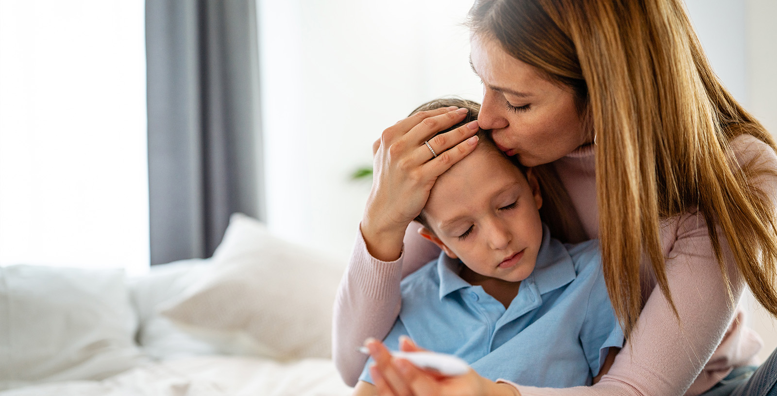 Mom kisses son's head while holding a thermometer