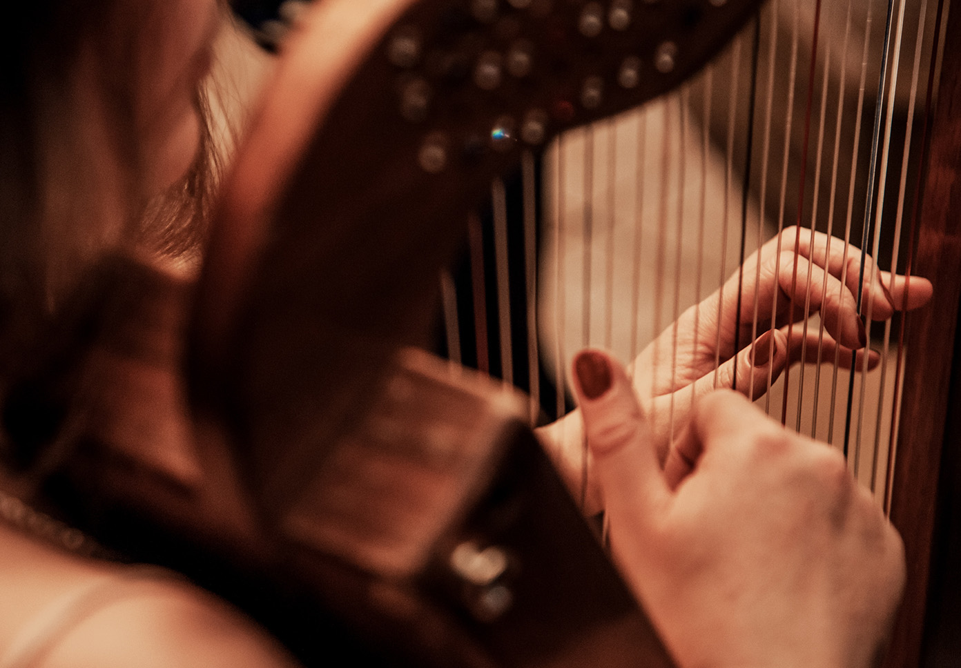 Looking over the shoulder of a harp player plucking harp strings