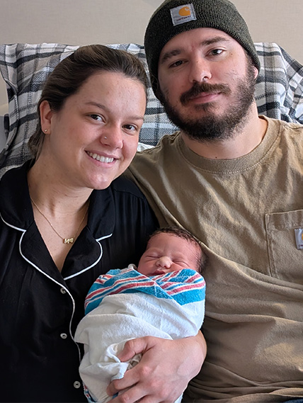 A mom and dad sit on a hospital bed holding their newborn baby