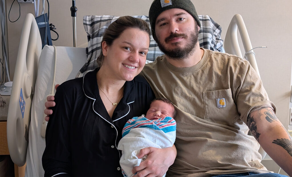 A mom and dad sit on a hospital bed holding their newborn baby