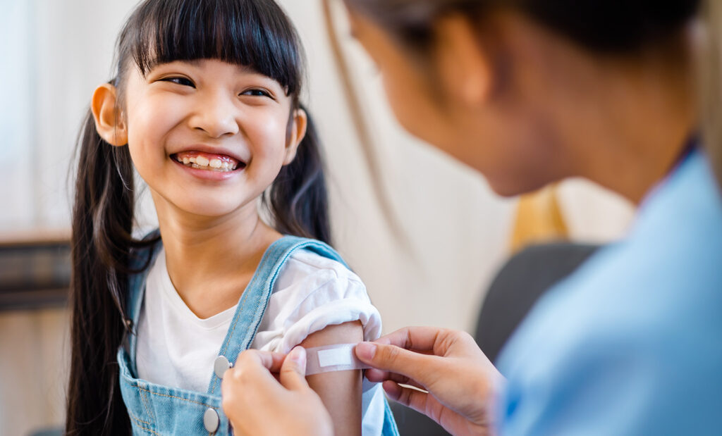 a girl smiles while a doctor puts a bandaid on her arm