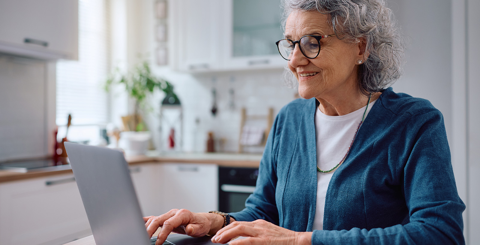 Woman wearing glasses sits in kitchen using a laptop