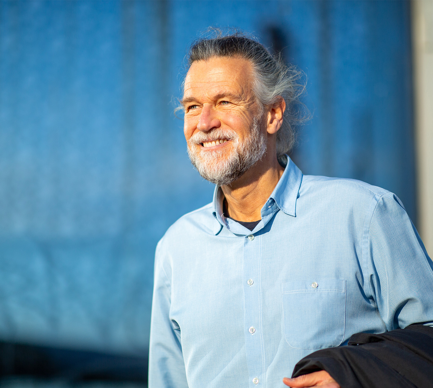 Older man with white hair and a beard smiles while walking outside