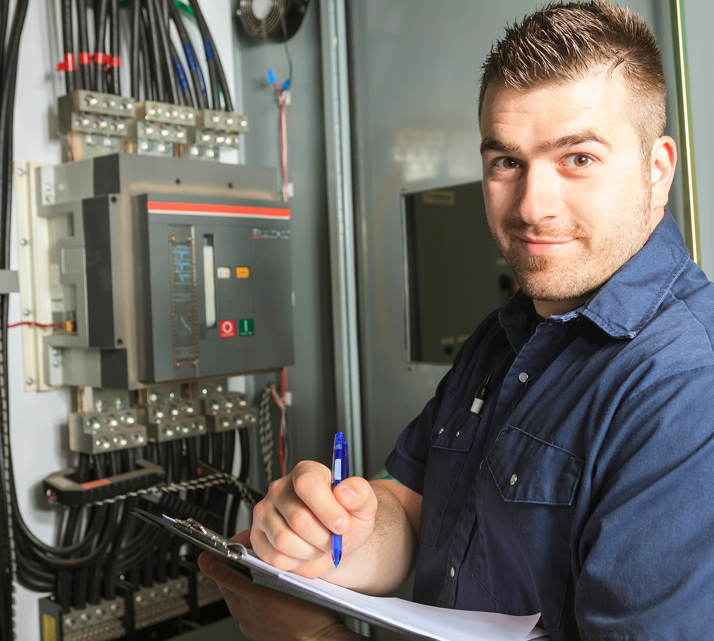 Electrician writes on a clip board in front of an open electrical panel