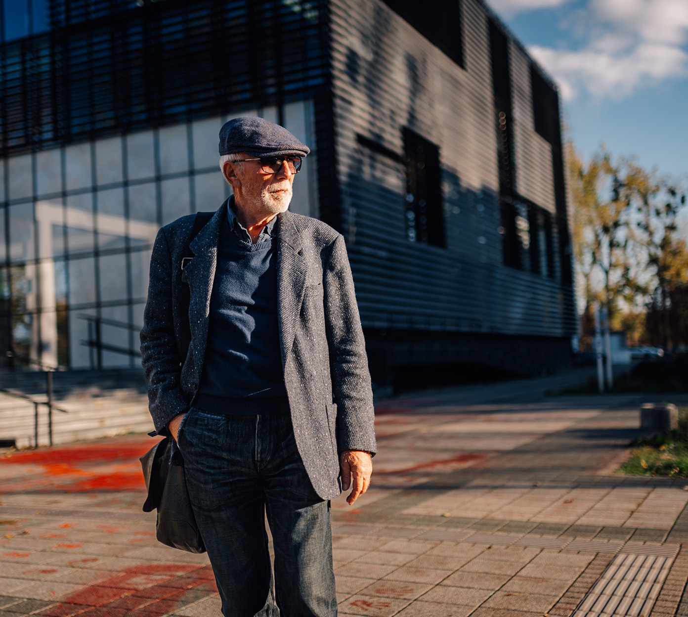 Older man wearing a beret walks outside in the sun