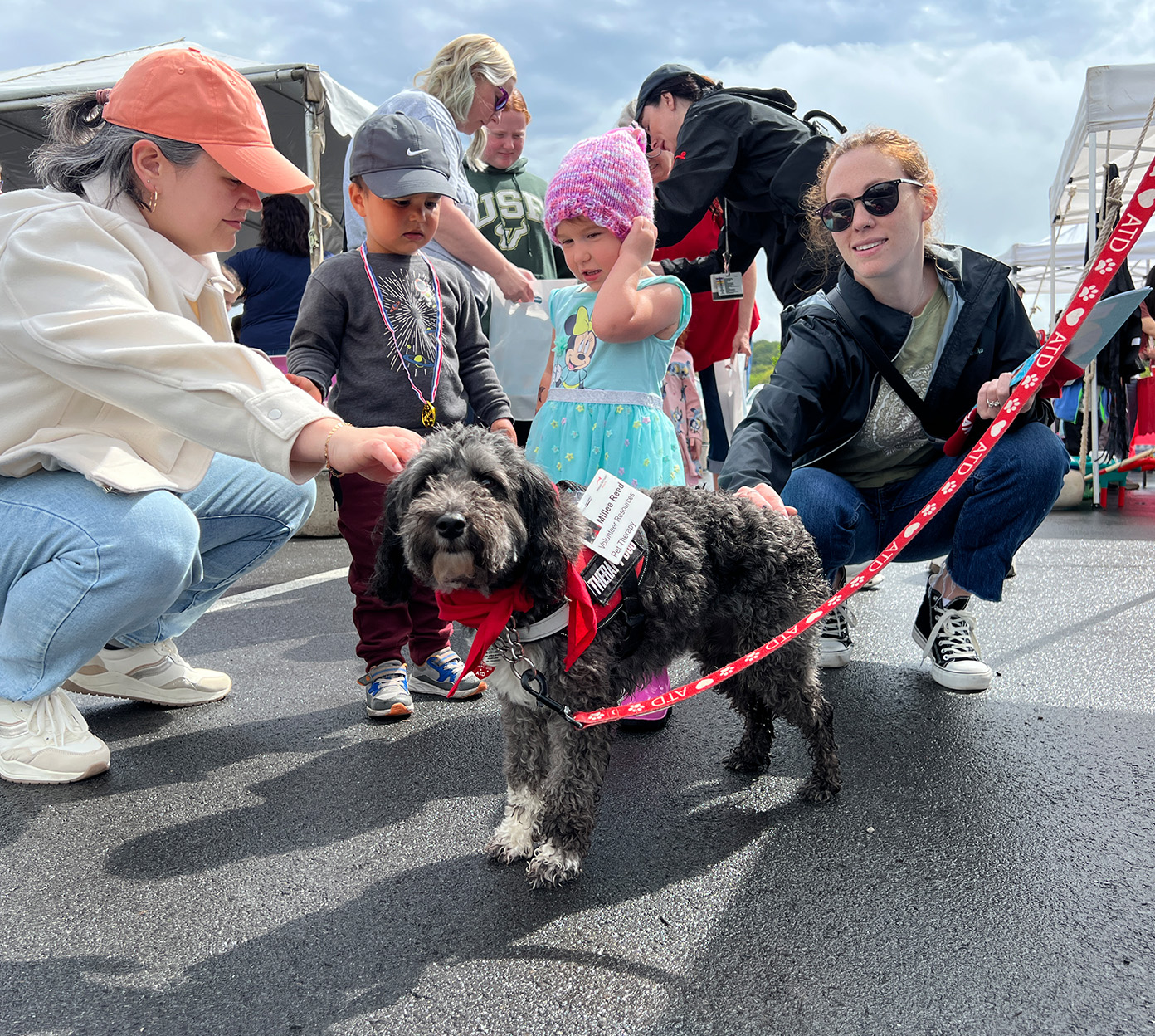 A mom and children kneel next to a therapy dog at Toftrees Community Day