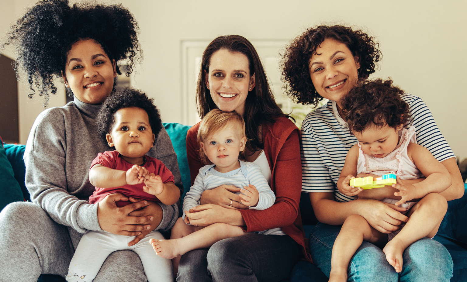 3 women sitting on couch holding babies and smiling
